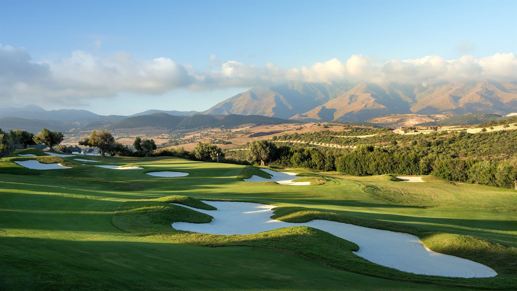 A golf course in the morning light: fairway, bunkers and the green against the hills.