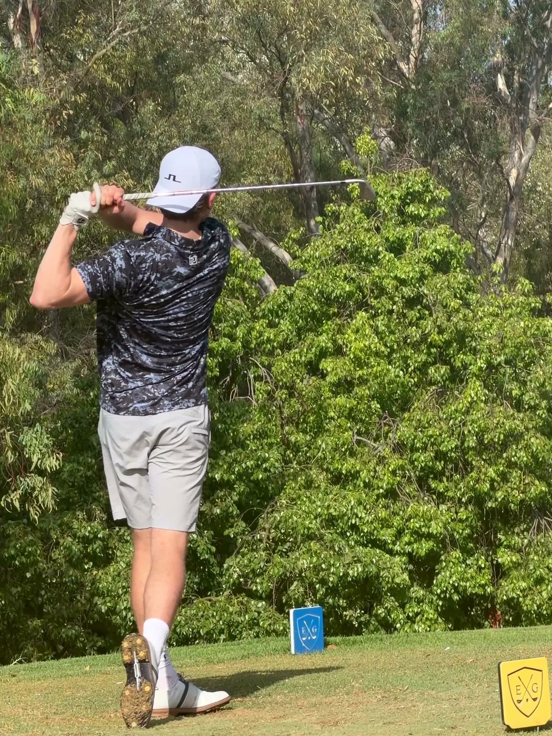 A golfer holding his follow-through, watching the ball down the fairway.
