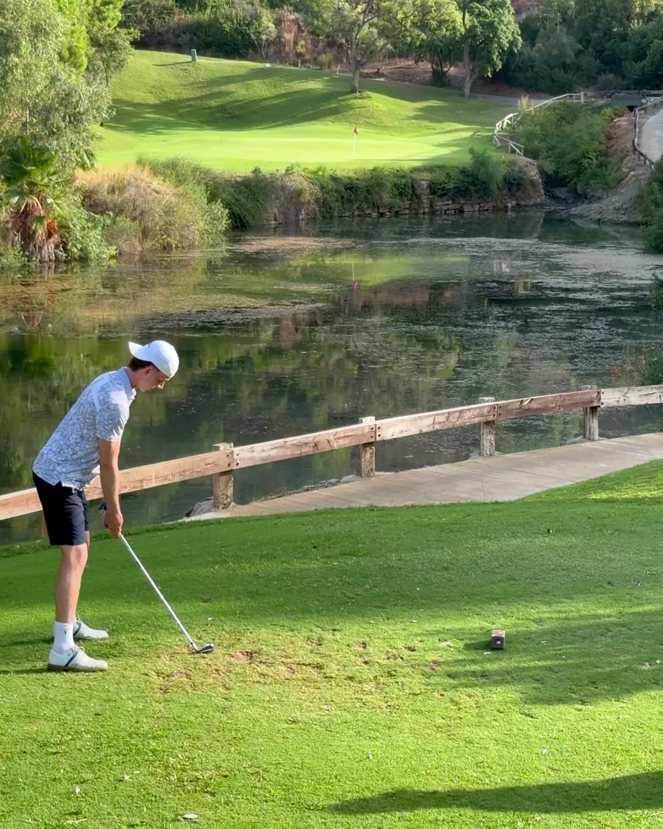 A golfer on the tee of a par 3, the pond and the green behind him.